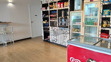 Espaço com máquinas de venda automática, diversas opções de lanches e bebidas, um refrigerador e uma vitrine de sorvetes Kibon.