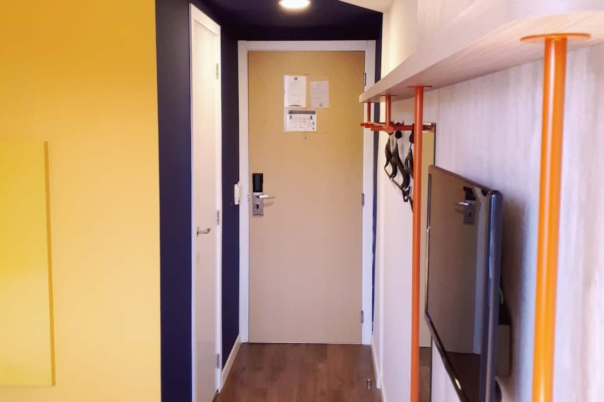 A hallway with a wooden floor, a yellow wall, a white door, and a mounted TV on the right.