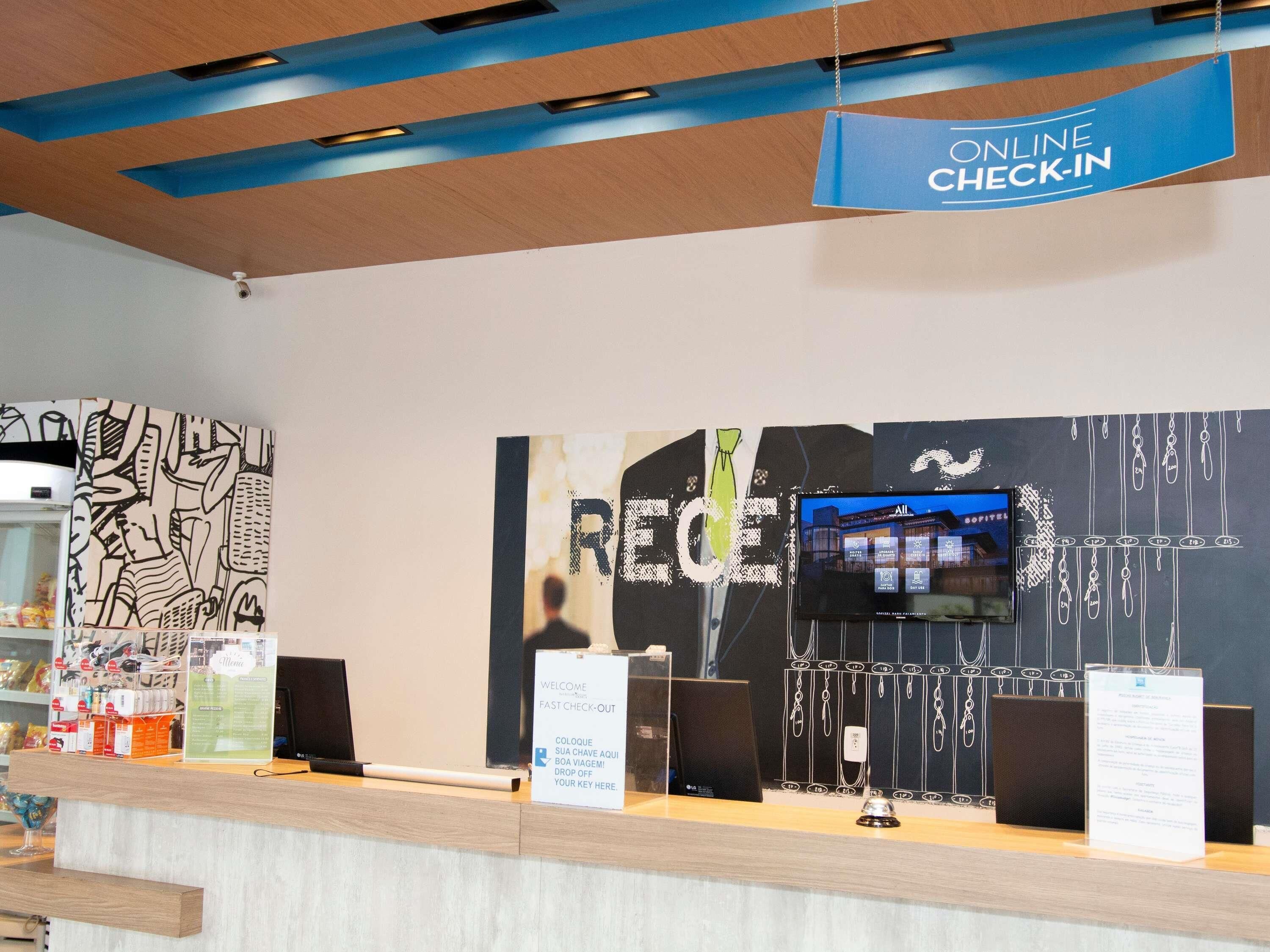 A hotel reception area with an online check-in sign, a large wall with abstract art, and a television displaying a building.