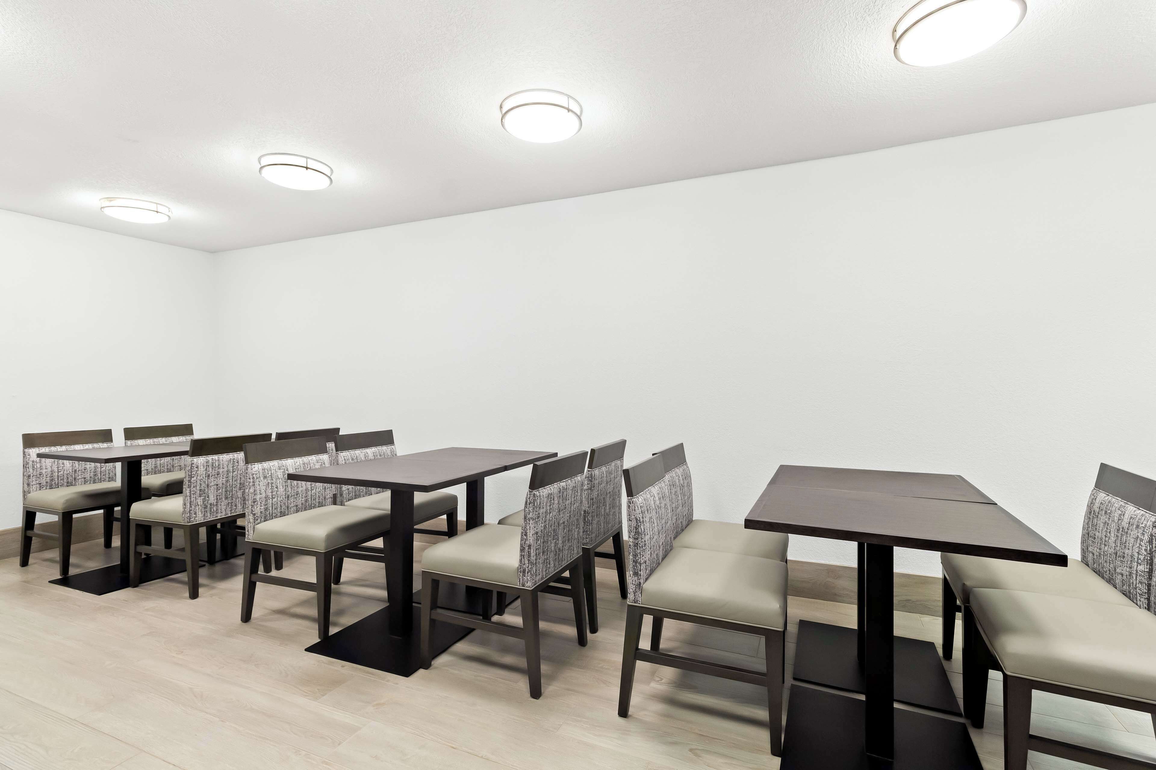 A dining area with multiple tables and chairs, recessed ceiling lights, and a plain white wall.