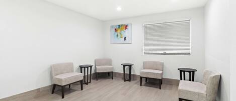 A room with five chairs and two small tables, white walls, and a wooden floor.