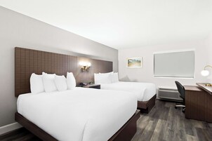 Habitación de hotel con dos camas, un escritorio, una silla, una mesita de noche, una lámpara de pared y un cuadro en la pared.