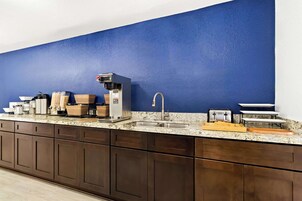 Una cocina con pared azul decorativa, una cafetera, un tostador y un lavamanos.