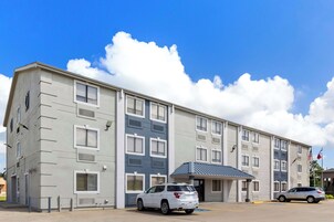 Un edificio de varios pisos con fachada plana, ventanas grandes y un estacionamiento con dos coches.