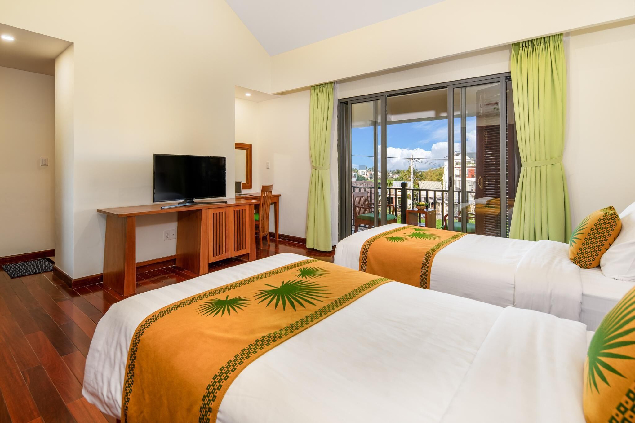 A hotel room with two beds, a TV, a desk, and a balcony with a view.