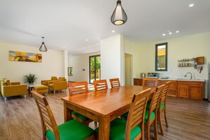 Un comedor moderno con una mesa y sillas de madera, una cocina con armarios de madera y una lámpara colgante.