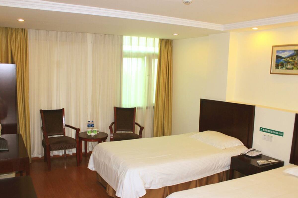A hotel room with two beds, a desk, a chair, a small table with water bottles, and a painting on the wall.