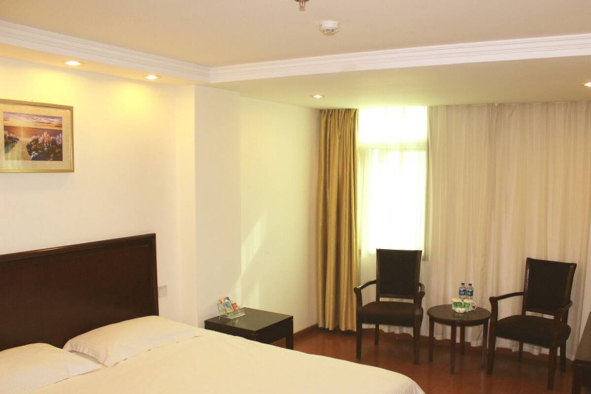 A hotel room with a large bed, two armchairs, a small table with a water bottle, and a painting on the wall.