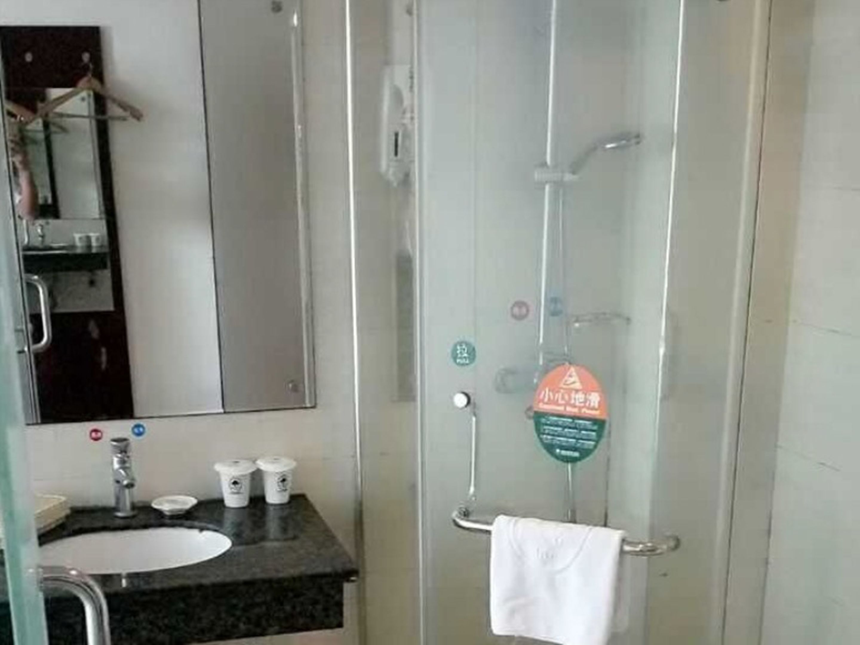 Un bagno con box doccia in vetro, un lavabo con piano d'appoggio scuro e uno specchio sopra al lavabo.