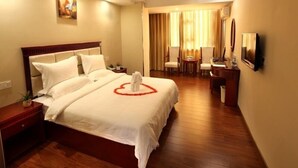 A hotel room with a large bed, a desk with a chair, a small table with a chair, and a TV on the wall.