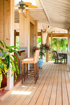 A wooden deck with a table and chairs, surrounded by potted plants and a ceiling fan.