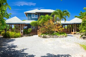 A two-story house with a covered porch, surrounded by tropical vegetation and a clear blue sky.