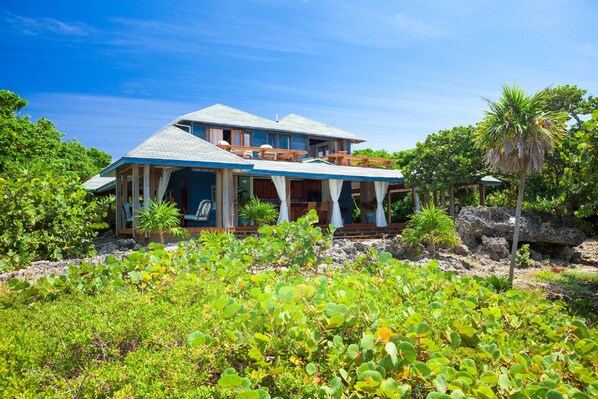 A two-story house with a balcony, surrounded by lush greenery and a clear blue sky.