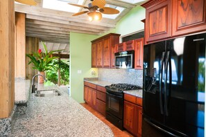 A kitchen with granite countertops, wooden cabinets, a black refrigerator, a microwave, and a stove.