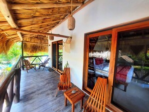 A wooden deck with thatched roof, wooden chairs, and a large sliding glass door leading to a room with a bed. - Casa Sofia Holbox (Isla Holbox)