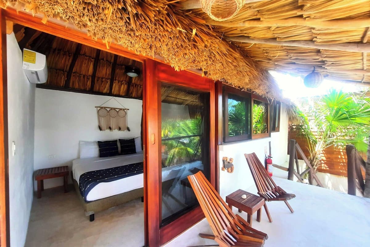 Una habitación con una cama, una mesita y dos sillas de madera.