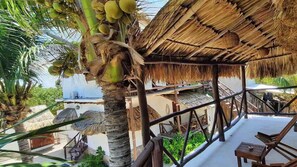 A thatched-roof structure with a balcony, palm trees, and a view of the sea. - Casa Sofia Holbox (Isla Holbox)