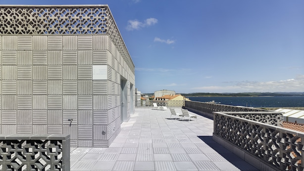 Une terrasse sur le toit avec une balustrade ornée, une vue sur la mer et un bâtiment en arrière-plan.