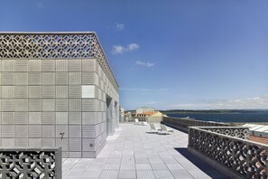 Une terrasse sur le toit avec une balustrade ornée, une vue sur la mer et un bâtiment en arrière-plan.