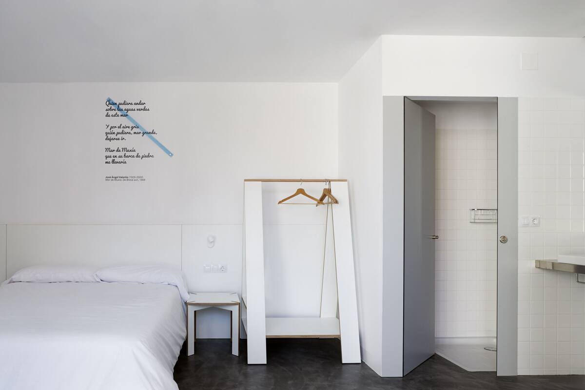 Ein modernes Hotelzimmer mit einem Bett, einem Sessel, einem Kleiderschrank und einem Badezimmer.