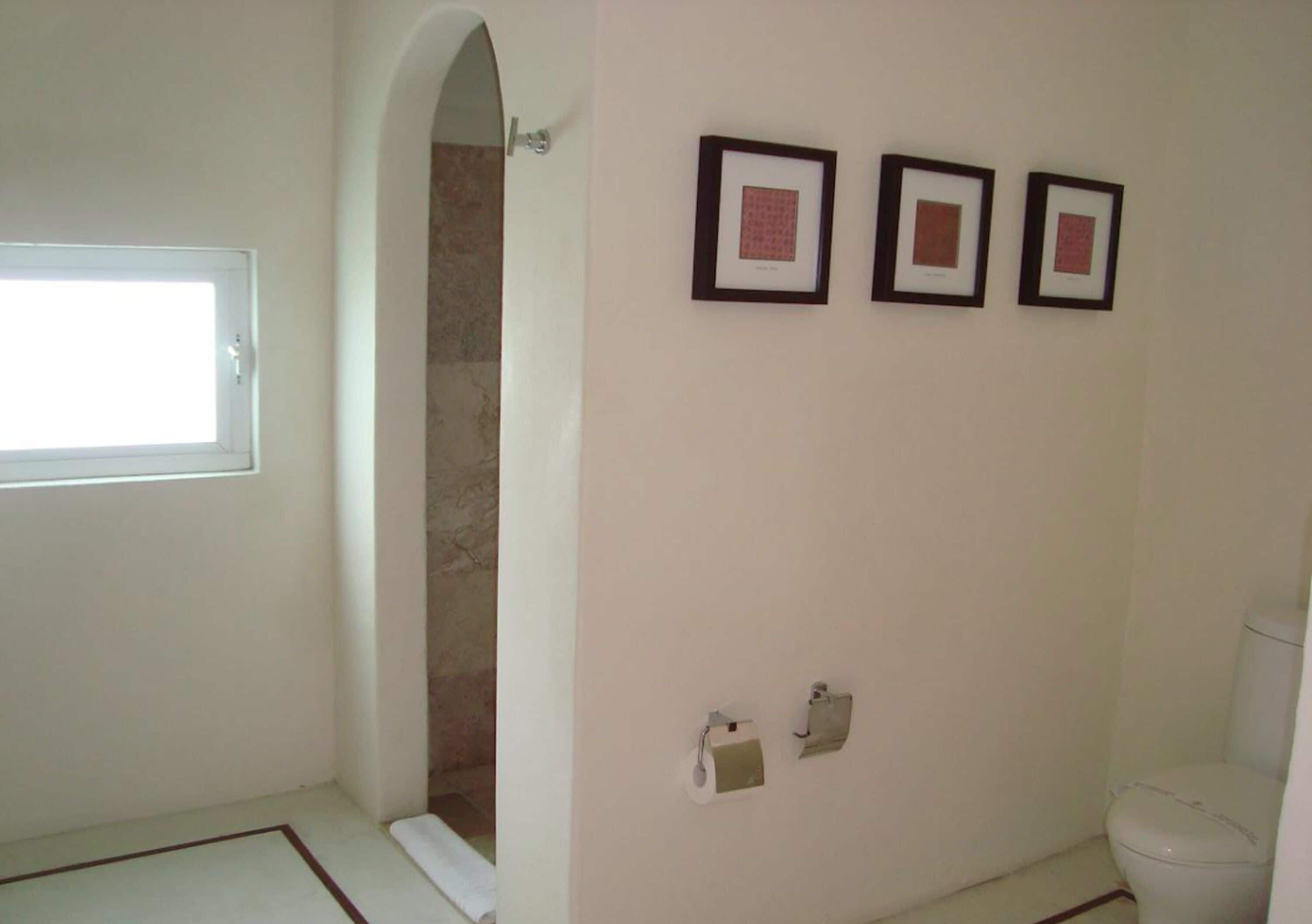 A bathroom with a toilet, a shower, and three framed pictures on the wall.