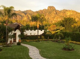 Un edificio blanco con techo de paja, rodeado por un jardín cuidado con un sendero de piedra que lleva a la entrada.