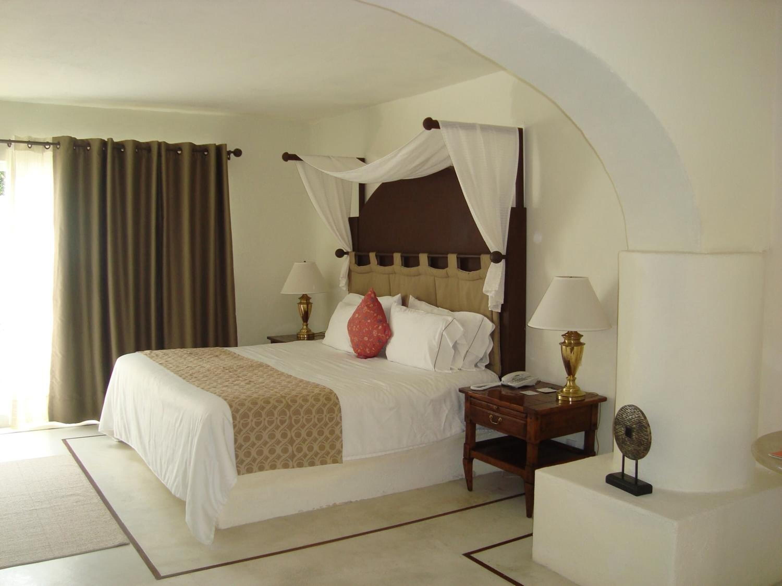 A hotel room with a four-poster bed, two bedside tables with lamps, a bedside phone, and a decorative mirror.