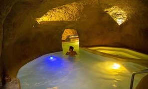 Una persona en una cueva rocosa natural con un estanque de agua, iluminada por luces artificiales.