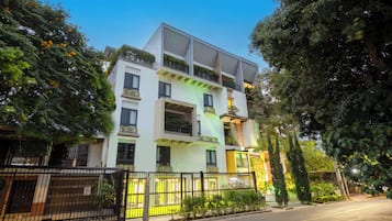 Um edifício residencial com vários andares, varandas, entrada com portão e áreas verdes ao redor.