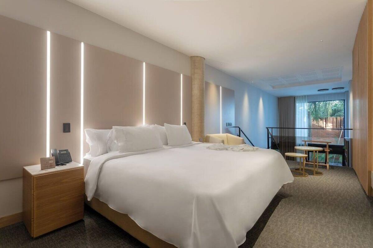 A modern hotel room with a large bed, bedside tables, a desk, and a balcony with a view.
