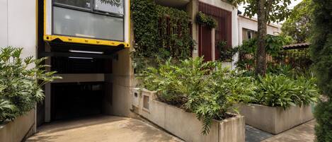 Fachada de hotel en amarillo y negro, macetas de concreto con plantas y una puerta visible.