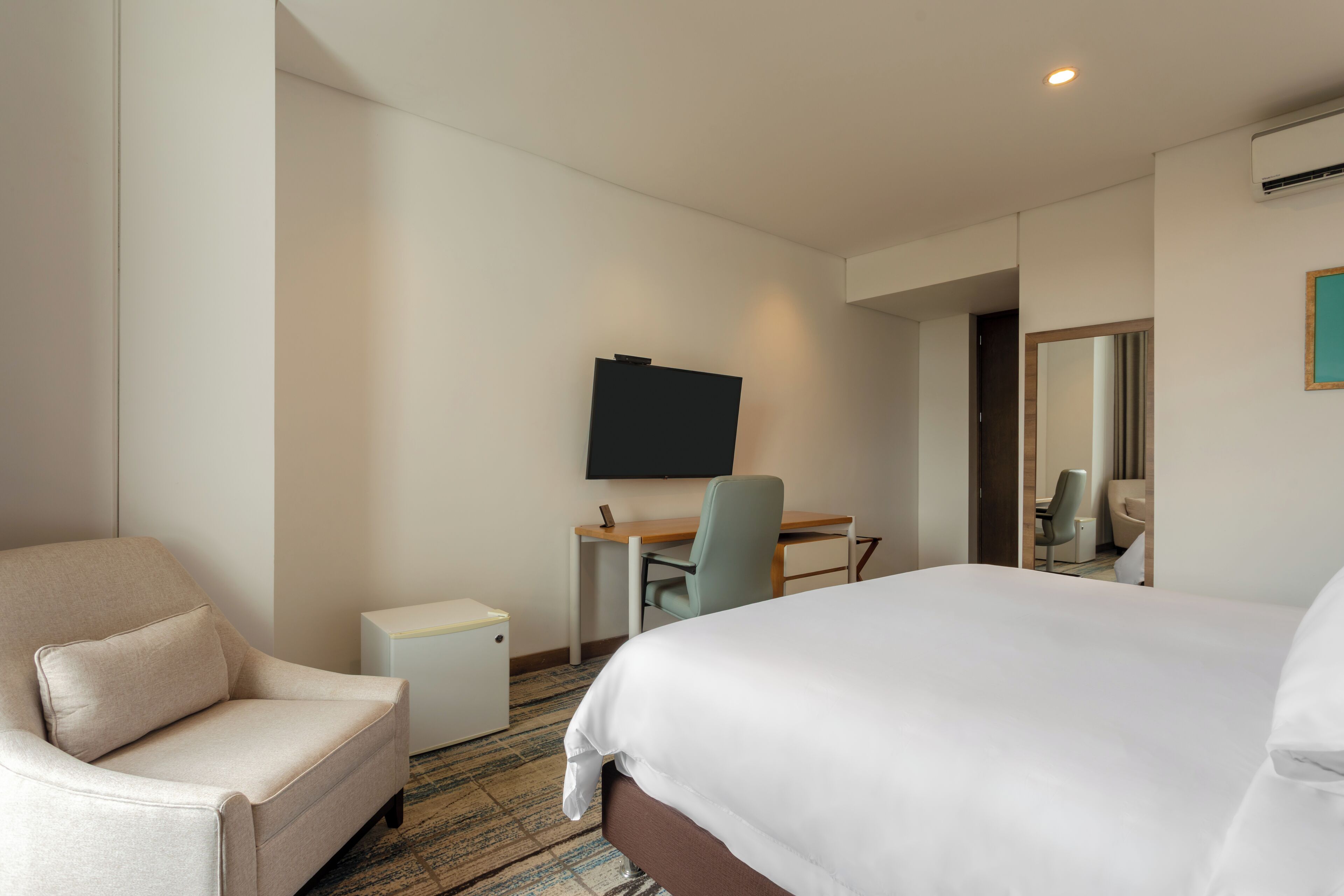 A hotel room with a bed, a desk, a chair, a small table, and a TV.