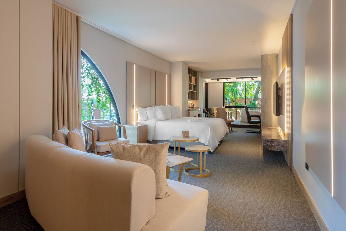 A modern hotel room with a large bed, a sofa, a small table, and a TV.