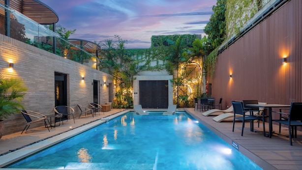 A swimming pool with lounge chairs and tables, surrounded by a brick wall and greenery. - Alko Hotel Integrado (Cali)