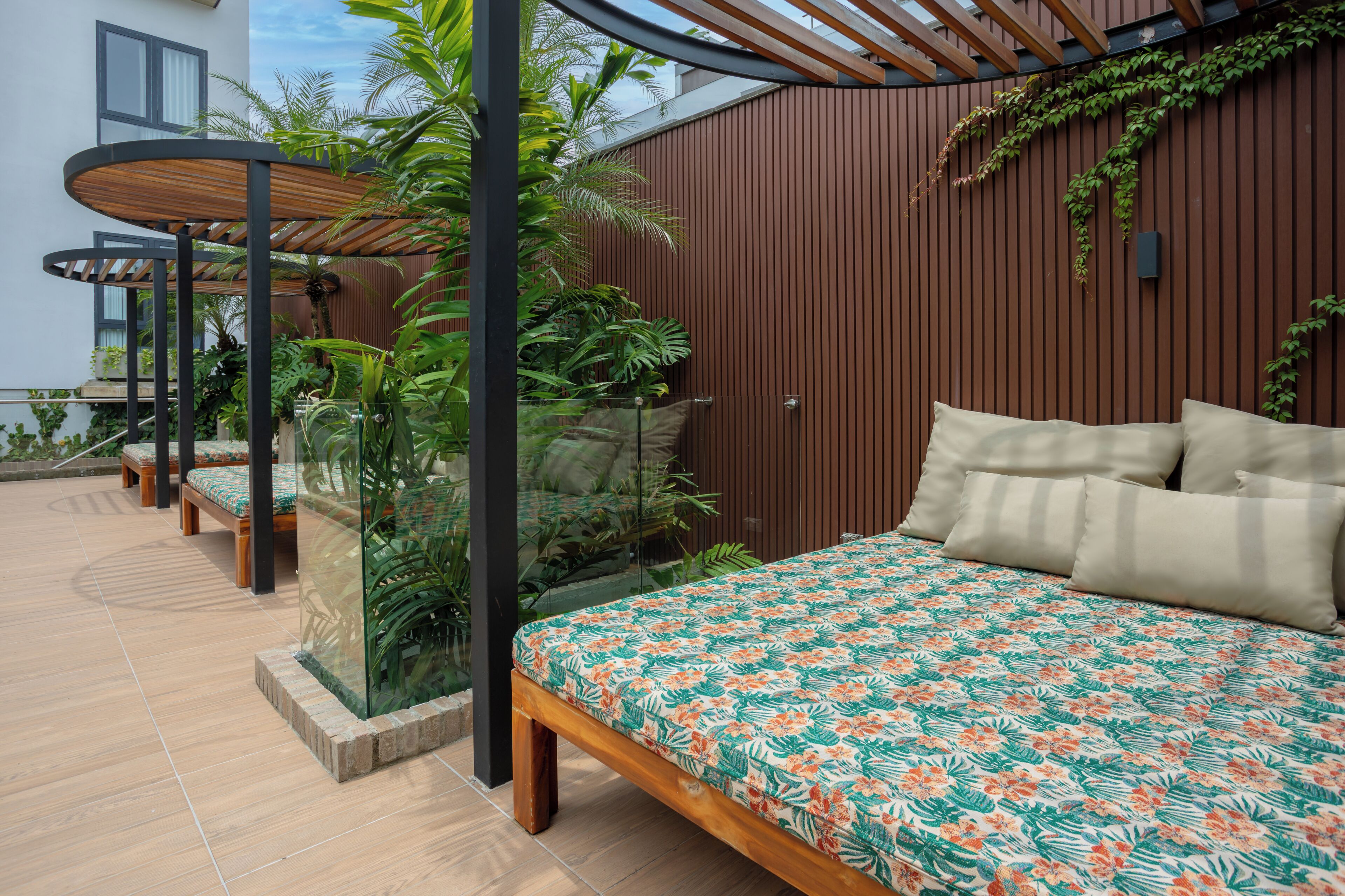 A bedroom with a bed, pillows, and a view of a garden with plants and a wooden wall.
