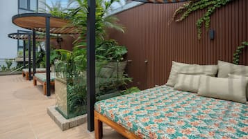 A bedroom with a bed, pillows, and a view of a garden with plants and a wooden wall.