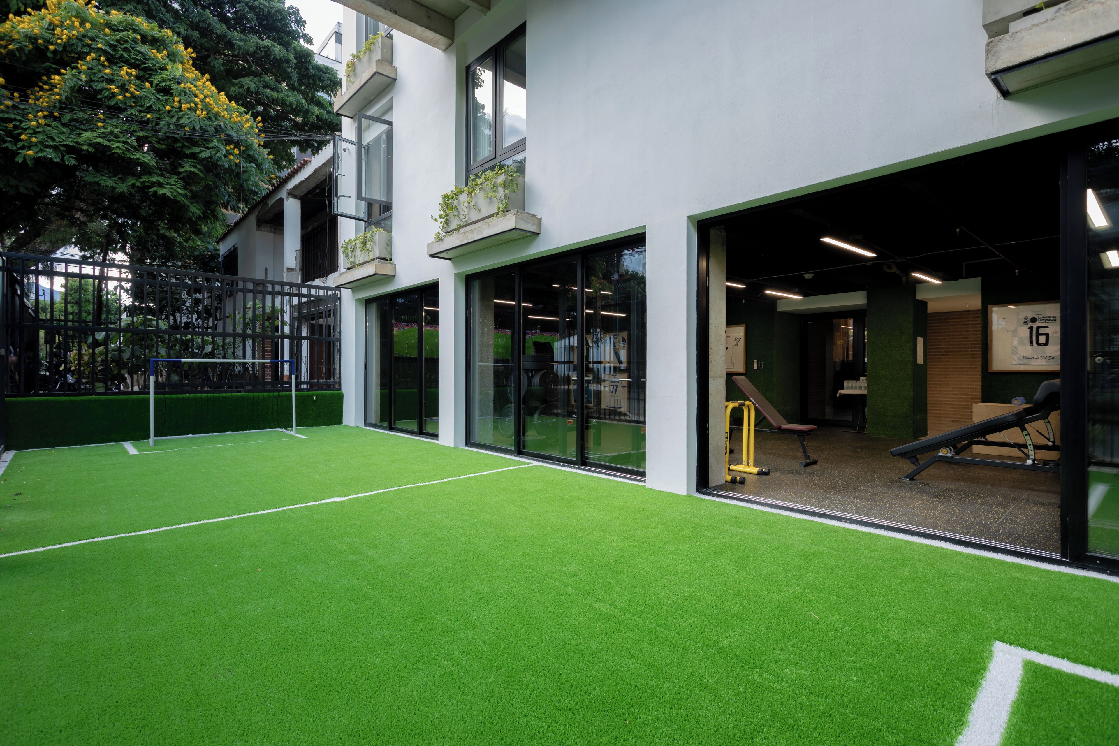 Instalación deportiva interior con césped artificial, una cancha de baloncesto y equipo de ejercicio.