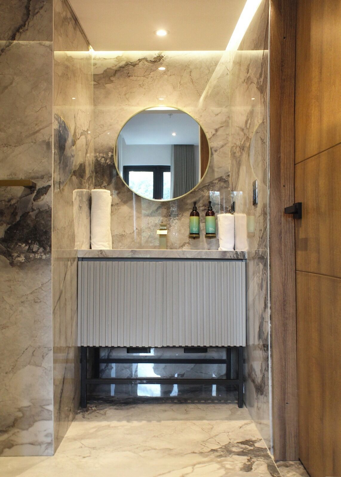 A bathroom with a marble wall, a round mirror, and a wooden door.