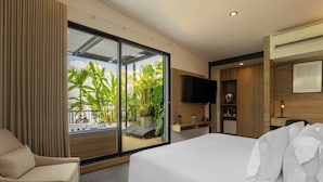 A modern hotel room with a large bed, a sofa, a TV, and a view of tropical plants through the sliding glass door. - Alko Hotel Integrado (Cali)