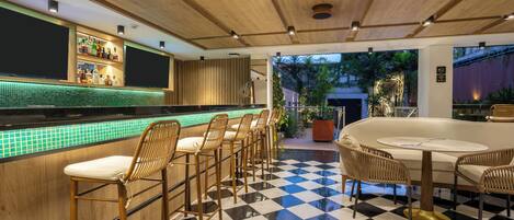 A bar area with a checkered floor, bar stools, a round table, and a tiled backsplash.