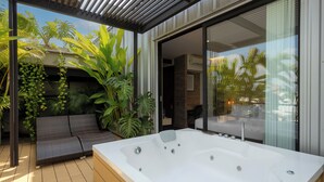 A modern outdoor hot tub area with a wooden deck, a cushioned seating area, and lush tropical plants. - Alko Hotel Integrado (Cali)