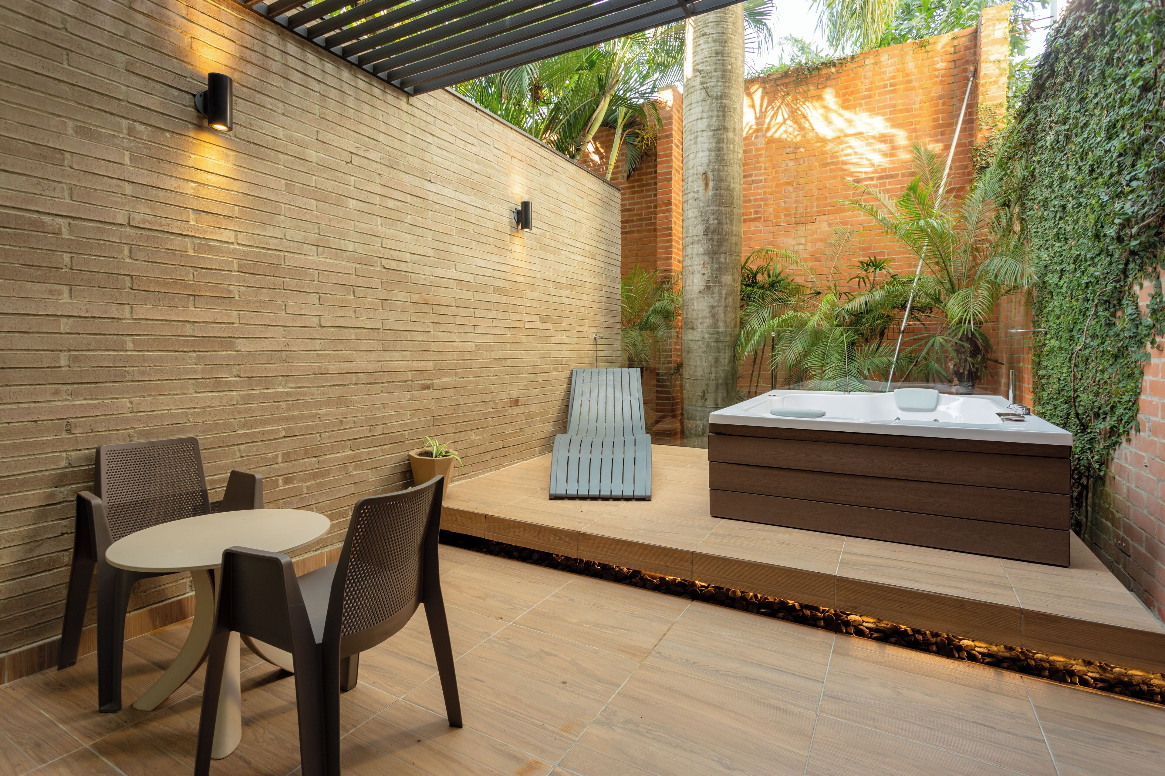 A patio with a brick wall, a wooden bench, a hot tub, and a table with chairs.
