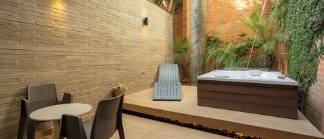 A patio with a brick wall, a wooden bench, a hot tub, and a table with chairs.