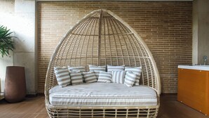 A wicker hanging chair with a cushioned seat and back, positioned against a brick wall. - Alko Hotel Integrado (Cali)