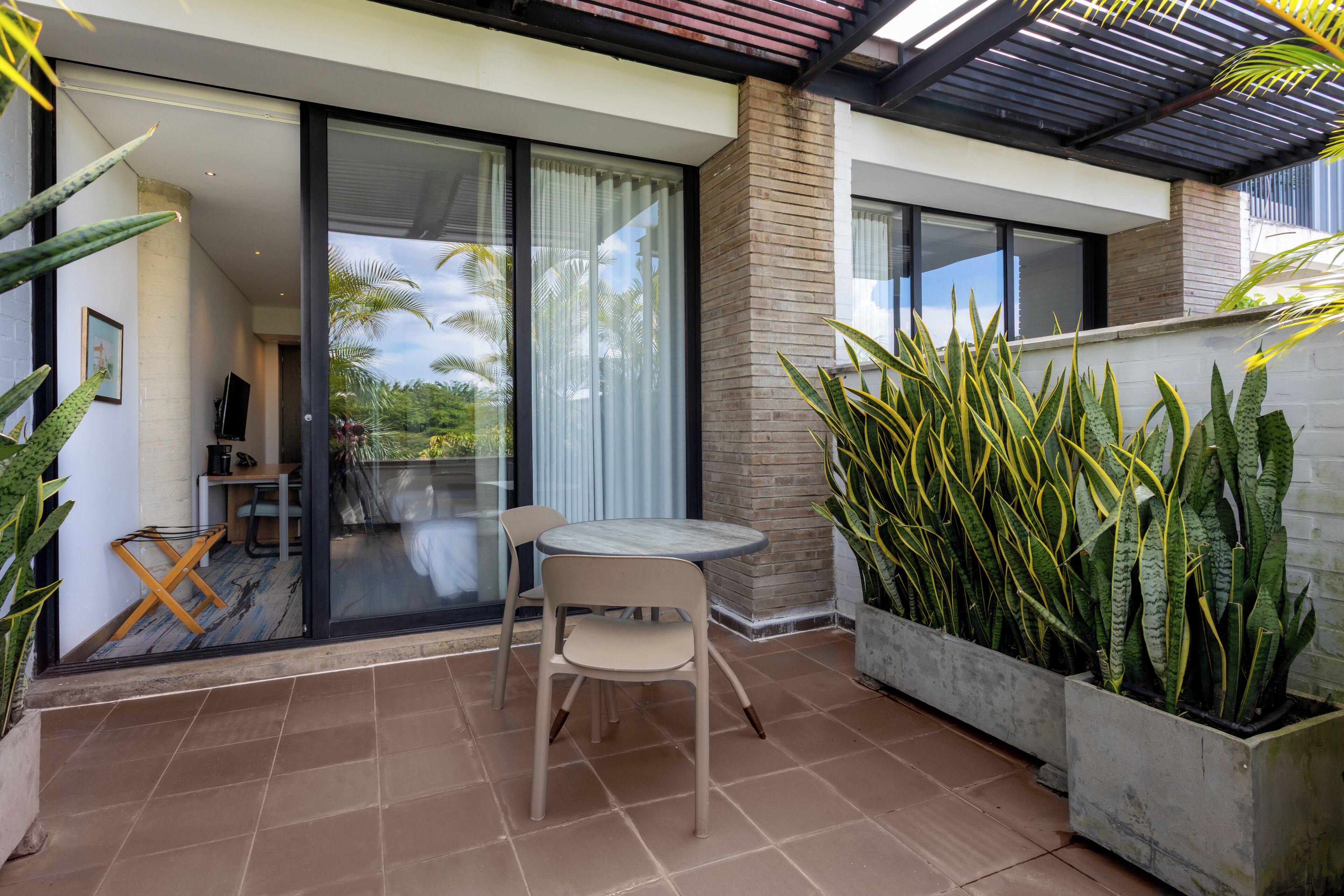 Eine moderne Außenpatio mit Tisch und Stühlen, eine Glastür zu einem Raum und große Kübelpflanzen.