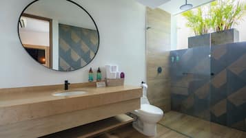 Un baño moderno con un espejo redondo, un lavabo y un inodoro. Cuenta con una zona de ducha con puerta de cristal y una planta en maceta.