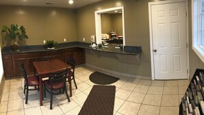 A kitchen with a dining table, chairs, a countertop, cabinets, a potted plant, a mirror, and a door. - Relax Inn of Medford (Medford)