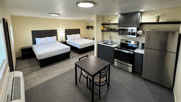 A compact hotel room with two beds, a small kitchenette, a dining table, and a window with blinds. - Relax Inn of Medford (Medford)