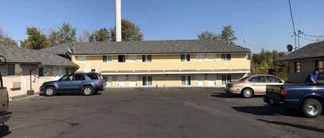 Un motel con un amplio estacionamiento, una chimenea alta y un edificio de dos pisos con varias habitaciones.