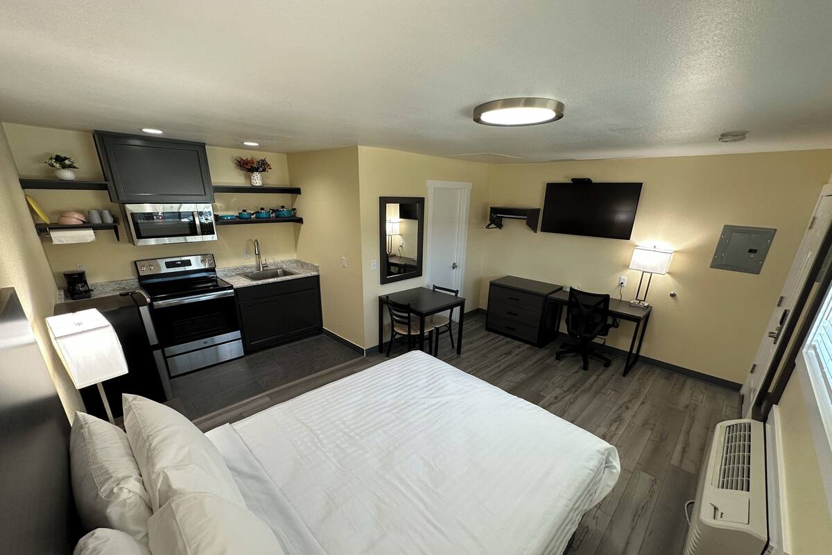 A hotel room with a bed, kitchenette, desk, and a TV.